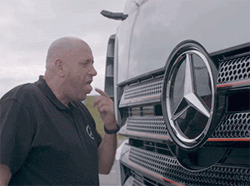 A Man Is Pointing At The Mercedes Logo On The Front Of A Truck . GIF