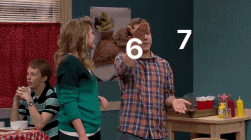 A Man Is Pointing At The Number 7 While Standing Next To A Woman GIF