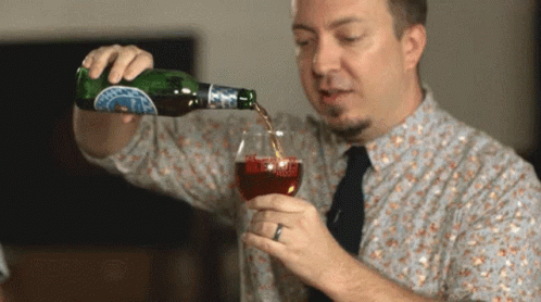 A Man Is Pouring A Drink From A Bottle Into A Glass With A Blue Label That Says ' A ' On It GIF