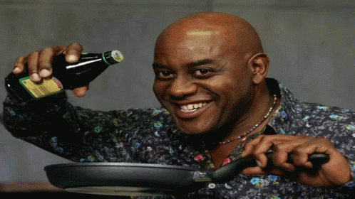 A Man Is Pouring Sauce Into A Frying Pan While Holding A Bottle GIF