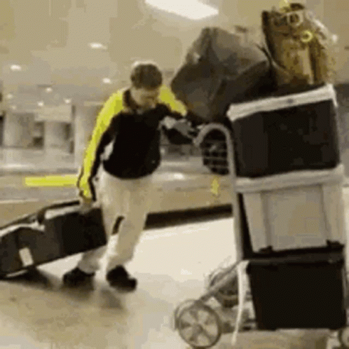 A Man Is Pushing A Cart Filled With Luggage And Boxes . GIF