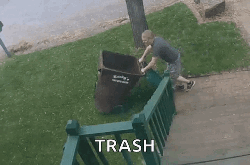 A Man Is Pushing A Trash Can Down A Sidewalk Next To A Railing . GIF