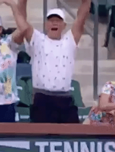 A Man Is Raising His Arms In The Air While Sitting In A Tennis Court . GIF