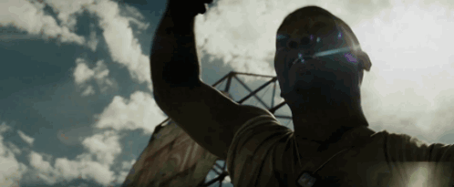 A Man Is Raising His Fist In The Air In Front Of A Blue Sky With Clouds . GIF