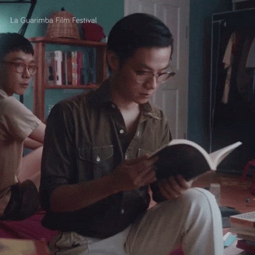 A Man Is Reading A Book With La Guarimba Film Festival Written On The Bottom GIF