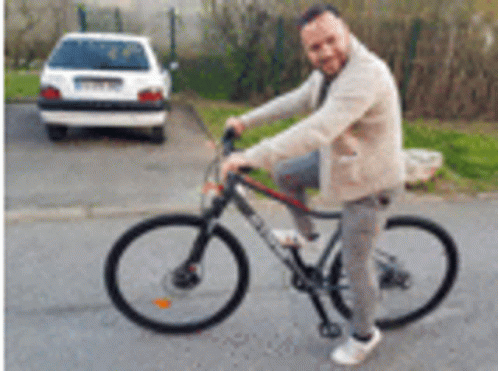 A Man Is Riding A Bicycle On A Street Next To A Car . GIF