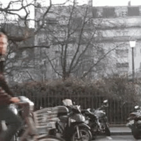 A Man Is Riding A Bike Down A Street In Front Of A Row Of Parked Motorcycles . GIF