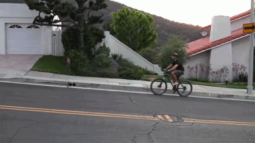 A Man Is Riding A Bike Down A Street With A Sign That Says ' No Parking ' On It GIF