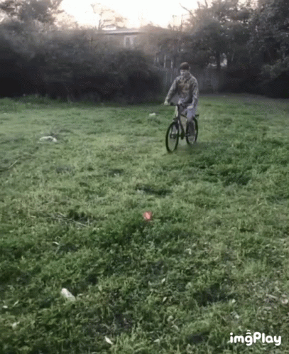 A Man Is Riding A Bike In A Grassy Field With The Hashtag Imgplay In The Lower Right Corner GIF