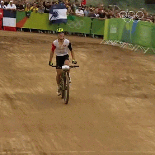 A Man Is Riding A Bike On A Dirt Track With A Crowd Behind Him GIF