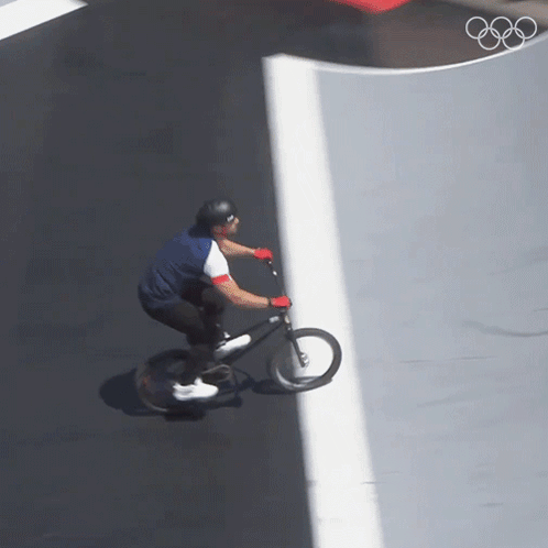 a man is riding a bike on a road with the olympic rings in the background