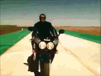 A Man Is Riding A Black Suzuki Motorcycle Down A Road GIF