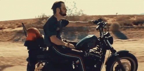 A Man Is Riding A Harley Davidson Motorcycle Down A Dirt Road GIF