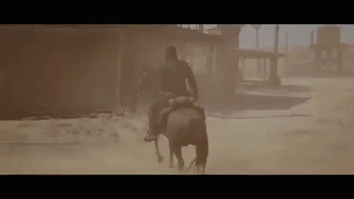 A Man Is Riding A Horse Through A Sandstorm In The Desert . GIF