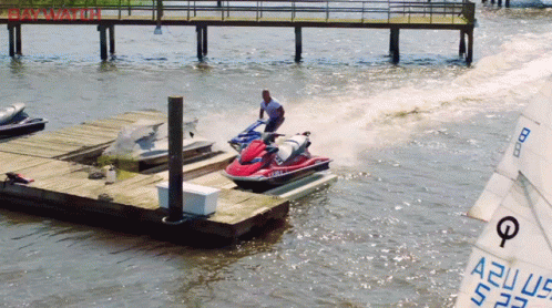 A Man Is Riding A Jet Ski In The Water Near A Dock GIF