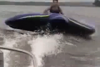 A Man Is Riding A Jet Ski Through A Flooded Area . GIF