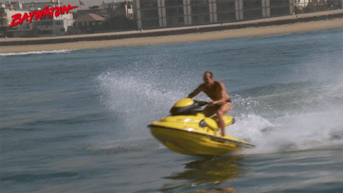 A Man Is Riding A Jet Ski With The Word Baywatch On The Bottom Right GIF