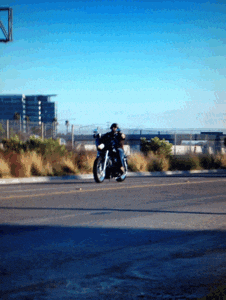 A Man Is Riding A Motorcycle Down A Road In A Parking Lot GIF