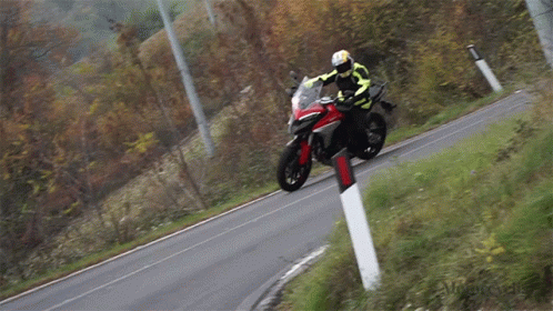 A Man Is Riding A Motorcycle Down A Road With A Red And Black Stripe On The Side GIF