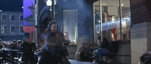 A Man Is Riding A Motorcycle Down A Street In Front Of A Store That Says Coca Cola GIF