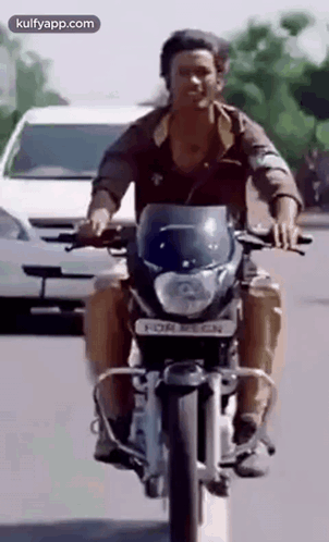A Man Is Riding A Motorcycle Down A Street Next To A White Car . GIF