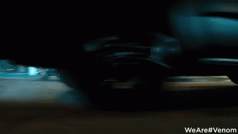 A Man Is Riding A Motorcycle Down A Street With A Sign That Says We Are #Venom GIF