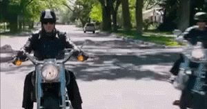 A Man Is Riding A Motorcycle Down A Street With Trees In The Background . GIF
