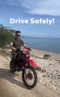 A Man Is Riding A Motorcycle On A Dirt Road With The Words Drive Safely Written Above Him GIF