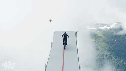 A Man Is Riding A Motorcycle On A Ramp With A Drone Flying Overhead GIF