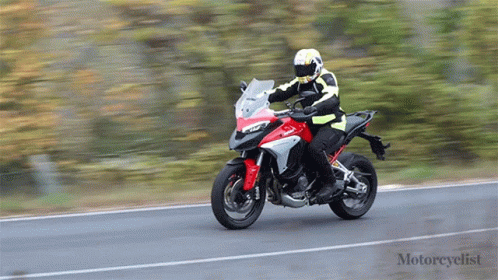 A Man Is Riding A Red And White Motorcycle On A Road GIF