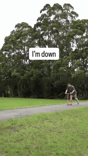 a man is riding a scooter down a path with trees in the background and a sign that says i 'm down
