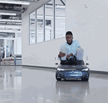 A Man Is Riding A Small Blue Car In A Hallway . GIF