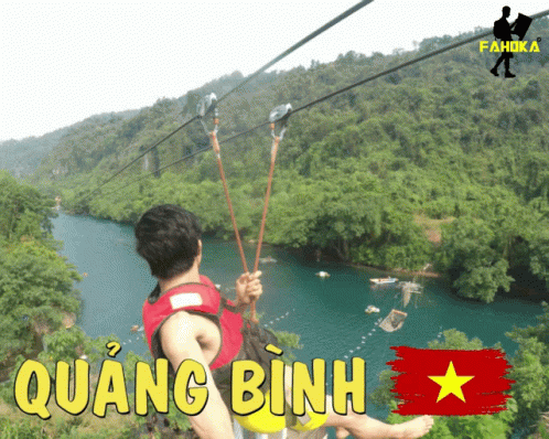 A Man Is Riding A Zip Line Over A River With Quang Binh In Yellow Letters GIF
