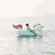 A Man Is Riding An Inflatable Unicorn In The Water . GIF