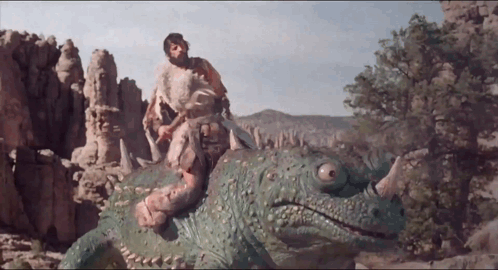 A Man Is Riding On The Back Of A Green Dinosaur With Horns GIF
