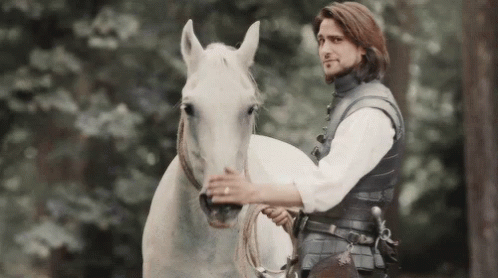 A Man Is Riding On The Back Of A White Horse In The Woods . GIF