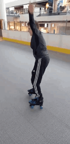 A Man Is Rollerblading On An Indoor Rink With His Arms In The Air . GIF