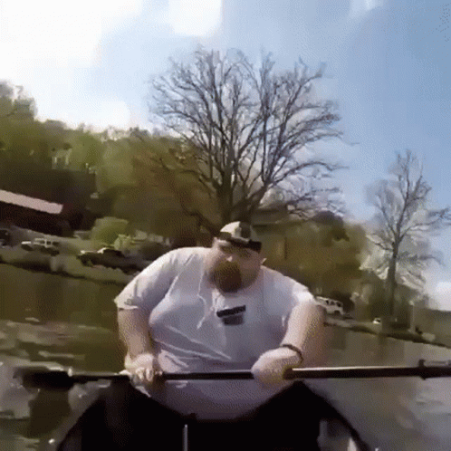 A Man Is Rowing A Boat On A River With A Tree In The Background GIF