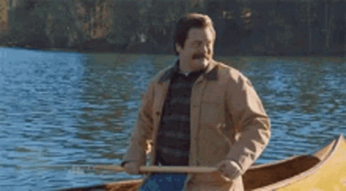 A Man Is Rowing A Canoe On A Lake With A Paddle . GIF