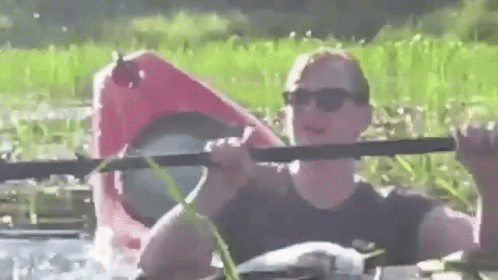 A Man Is Rowing A Red Kayak In A River . GIF