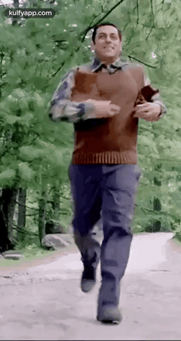A Man Is Running Down A Dirt Road In The Woods . GIF