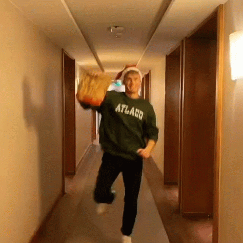 A Man Is Running Down A Hallway Wearing A Green Sweater That Says Atlaco GIF