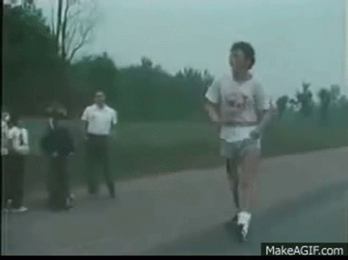 A Man Is Running Down A Road With A Group Of People Watching . GIF