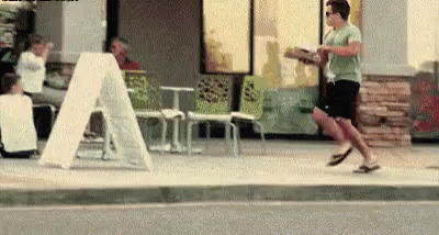 A Man Is Running Down A Sidewalk Holding A Box Of Pizza . GIF
