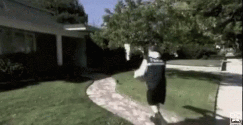 A Man Is Running Down A Sidewalk In A Yard . GIF
