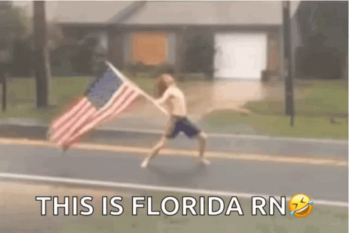 A Man Is Running Down A Street Holding An American Flag . GIF