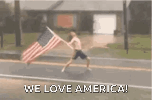 A Man Is Running Down A Street With An American Flag . GIF