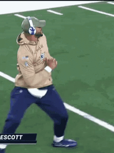 A Man Is Running On A Football Field Wearing Headphones . GIF