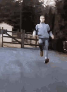 A Man Is Running On A Road With A Fence In The Background . GIF