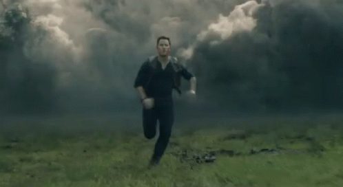 A Man Is Running Through A Field With Smoke Coming Out Of It . GIF